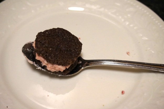 Sandwich cookie sitting on a teaspoon for size comparison.